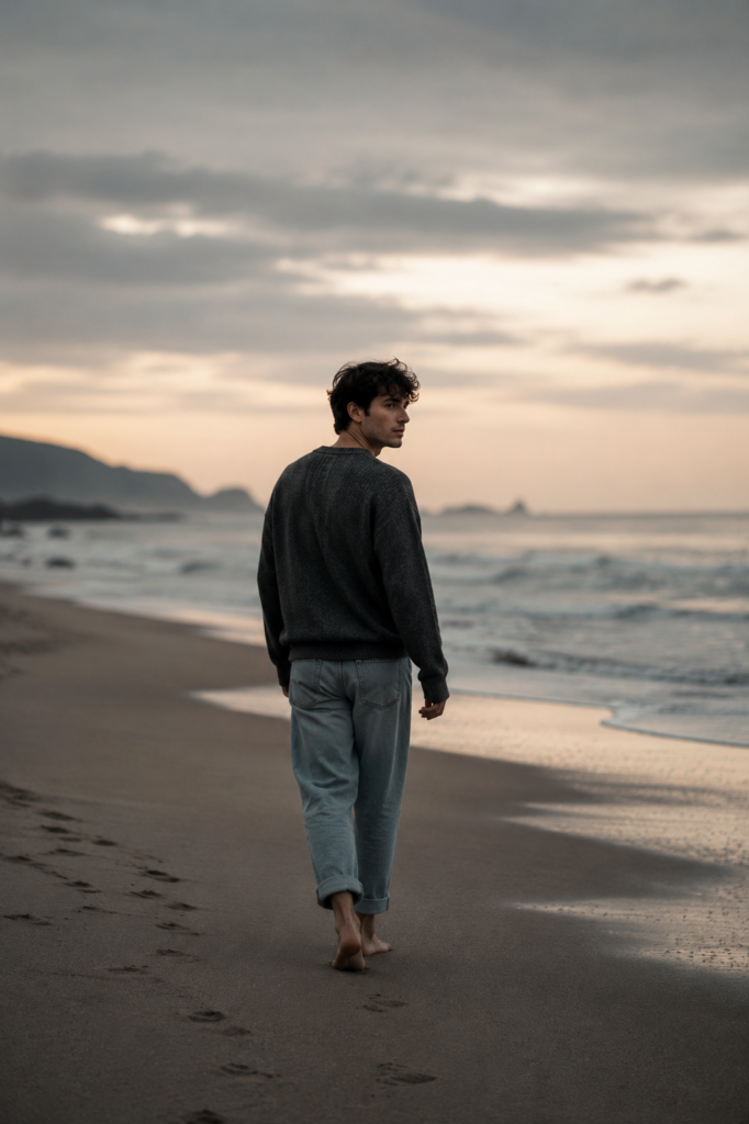 Homem caminhando sozinho pela praia enquanto olha para trás com expressão melancólica, simbolizando a culpa emocional de seguir em frente após uma relação.