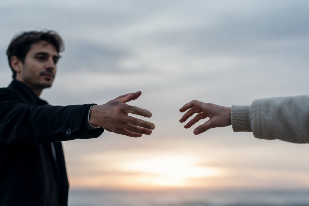 Homem estendendo lentamente a mão em direção à mão de outra pessoa, sem que elas se toquem, simbolizando o desejo de criar um novo vínculo enquanto ainda existe medo de se envolver novamente.